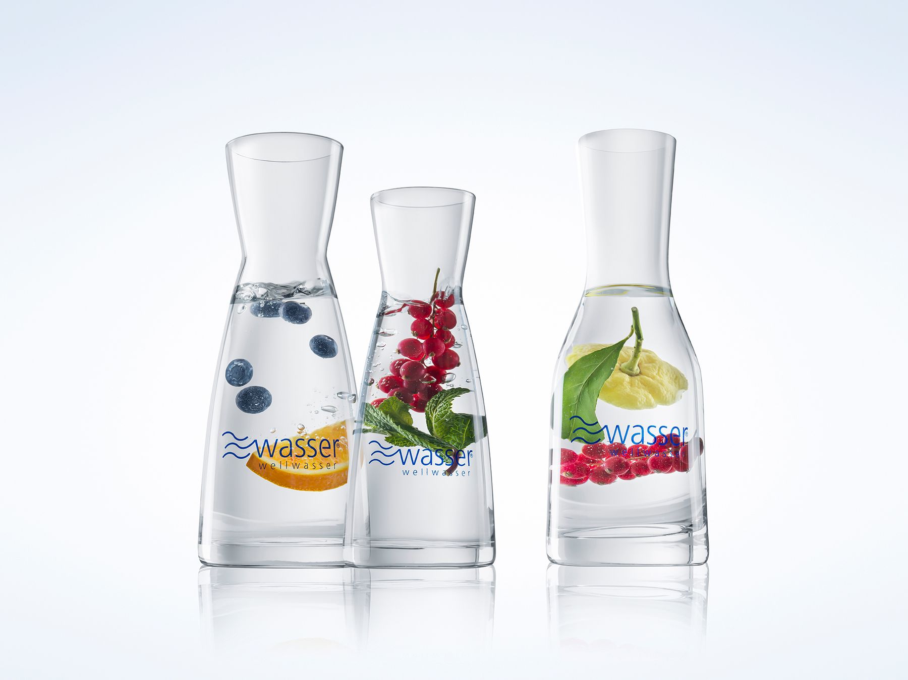 Drei Glaskaraffen mit infundiertem Wasser: Heidelbeeren und Orange, rote Johannisbeeren und Minze sowie Zitrone mit roten Johannisbeeren.